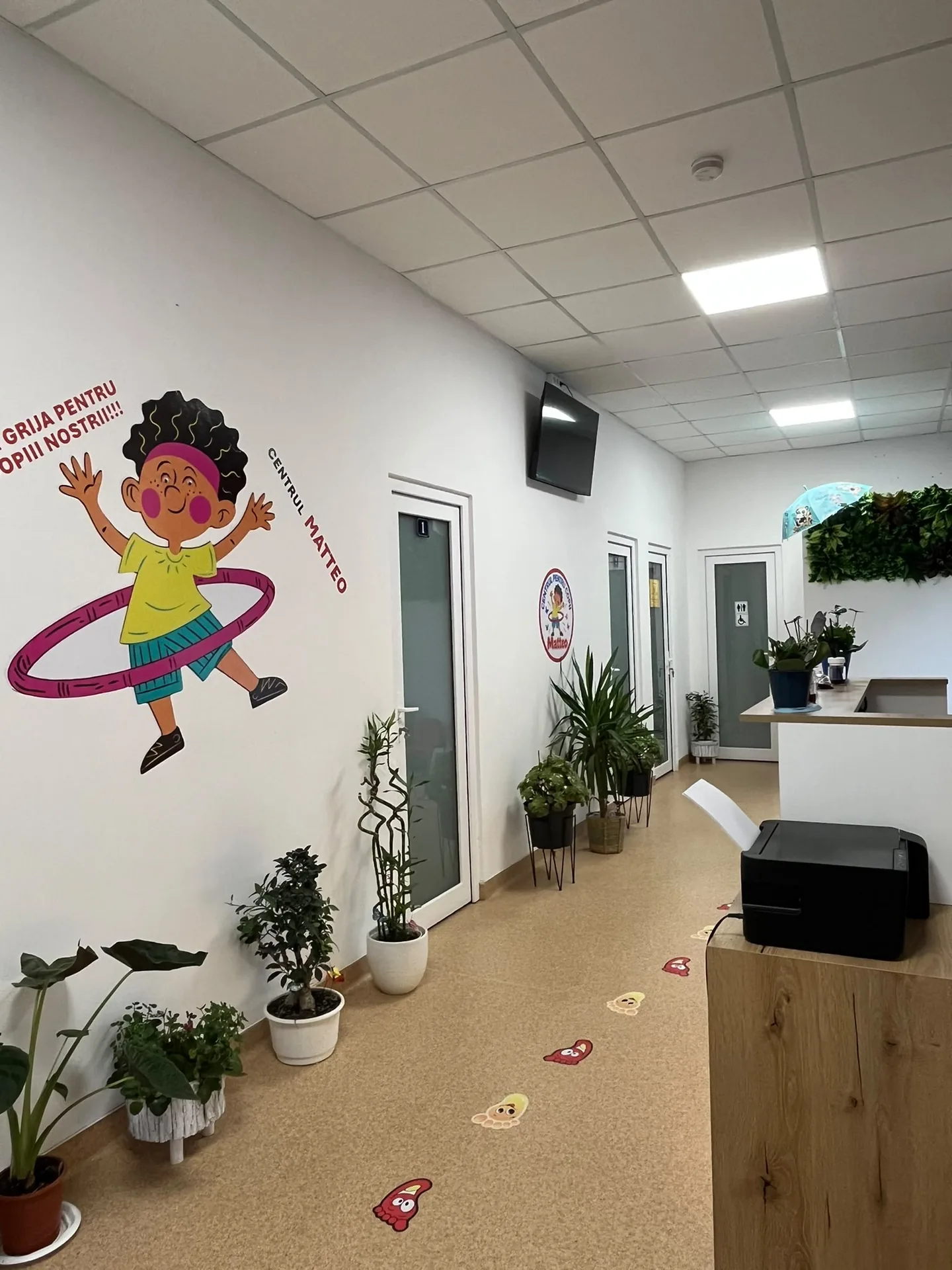 Holul Centrului Matteo, cu plante, uși către camere și biroul de recepție.